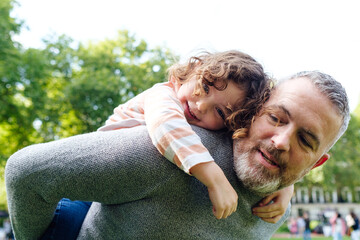 Close up Father giving a daughter piggyback ride when playing in the park.