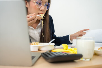 Busy and tired businesswoman eating spaghetti for lunch at the Desk office and working to deliver...