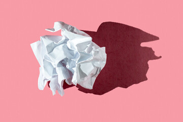 Crumpled white paper ball on a pink background with hard light