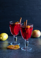 Two glasses of mulled wine, spices, fruits, dried oranges on dark background