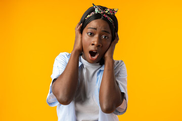 Stunned African female with mouth opened realizes bad news against yellow background