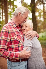 Loving Retired Senior Couple Hugging On Walk In Woodland Countryside Together