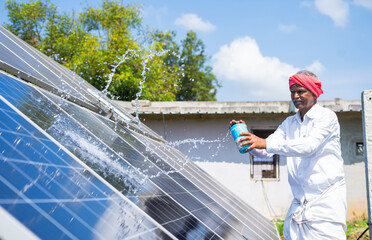 Indain Village farmer cleaning with water on solar panels at farmland - concept of renewable...