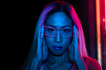 Closeup portrait of young pretty woman with naked shoulders in red neon light on dark background. Art, creativity, fashion, style