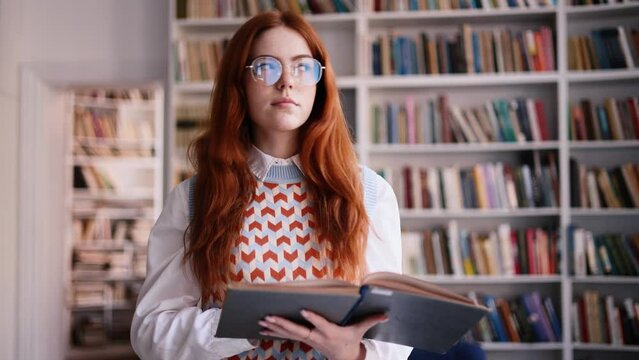 Beautiful red haired girl with freckles reading a book and asking to be quiet with serious look at university library. 