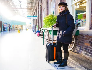 Adult woman dragging suitcase throughout a train station. © kikearnaiz