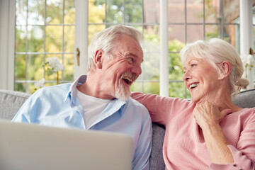 Retired Senior Couple Sitting On Sofa At Home Using Laptop