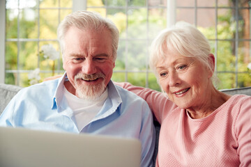 Retired Senior Couple Sitting On Sofa At Home Using Laptop