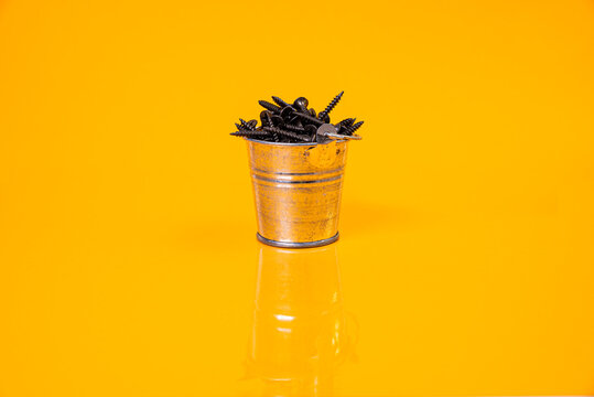 Many metal self-tapping screws made of steel in a glass, in bucket jar. self-tapping screw for metal, for iron, chrome-plated self-tapping screw, on an orange yellow background,