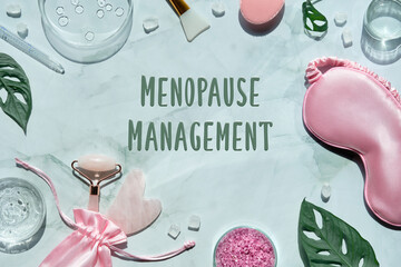 Menopause management text on wellness flat lay. Pink stone facial roller and guasha stone on mint...