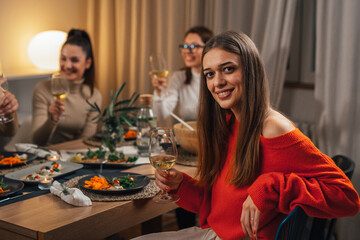young adult woman sitting table on home dinner party holding glass of wine and looking at camera