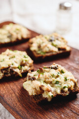 Rye bread toast with smoked mackerel, cream, cheese and green onion on wooden cutting board. Delicious appetizer, tapas. Selective focus - 544612154