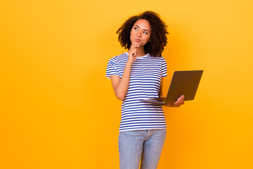 Photo of pretty minded girl hand touch chin look empty space hold netbook isolated on yellow color...