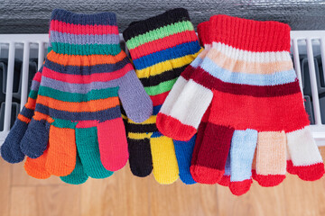 Warm colorful child's gloves on the radiator heating. Heating season at home, warm clothing, concept.