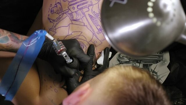 Close-up of a man with black gloves doing a tattoo on the leg of a young woman. Professional artist making tattoo in salon.