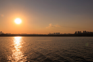 Naklejka premium Orange sunset sky and sun over the sea. Water surface and outlines on the horizon.