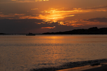 Orange sunset sky and sun over the sea. Water surface and outlines on the horizon.