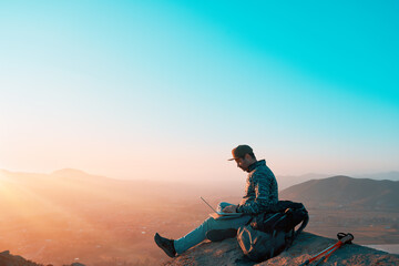 mature latin man on top of the hill with a laptop working outdoors at sunset over the valley 