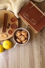 Cup of tea or coffee, various spices, bowl of cookies, tangerines, books, reading glasses and knitted blanket on wooden table. Hygge at home concept, flat lay.