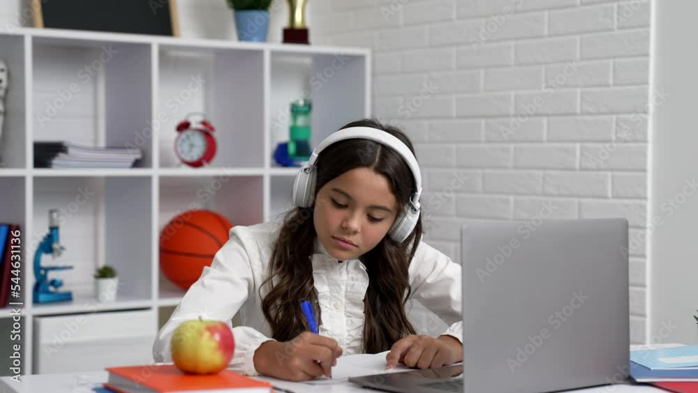 Wall mural serious teen girl in headphones writing at school online lesson with laptop, education online