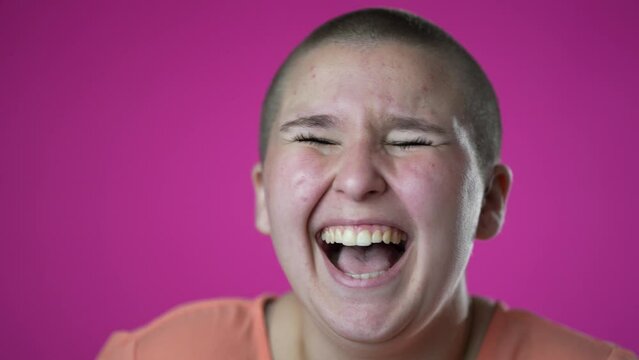Closeup slow motion laughing and smiling gender fluid woman 20s years old posing isolated on pink background studio. People sincere emotions lifestyle concept. Looking at camera with charming smile