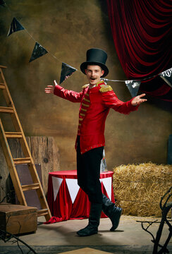 Vintage portrait of male retro circus entertainer expresses rejoice and announces start of show over dark retro circus backstage background.