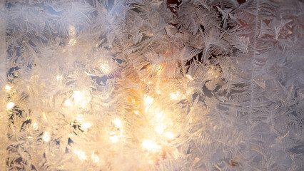 Abstract winter background of frozen glass, through which the lights of the garland glow. Condensation of moisture at extreme temperatures. Beautiful texture of nature.
