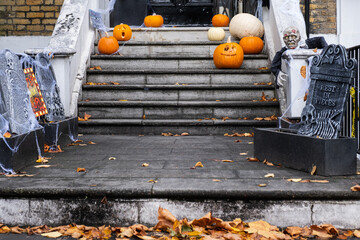 Halloween decorations of traditional english house. Curved pumpkins, skeletons and graves on the doorstep.