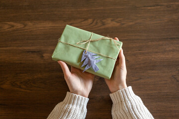 First person top view of woman hands holding craft paper gift box on wooden table