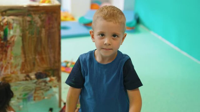 cute blond-haired boy waving at the camera and smiling, medium shot kindergarten. High quality 4k footage
