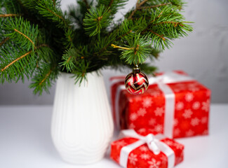 Festive composition with Christmas tree branches in a vase and gift boxes. Gifts for the New Year and Christmas. Christmas tree decoration. Selective focus.