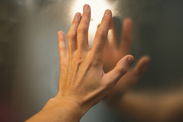 A man's hand touches the misted mirror in the bathroom. The reflection of a man's palm and fingers in a fogged mirror. Blurring with your finger as a background in a mirror image.