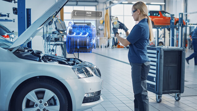 Female Mechanic Uses a Tablet Computer with an Augmented Reality Diagnostics Software. Specialist Inspecting Car's V6 Engine in Order to Find Broken Components. Hi-tech Car Service. - Powered by Adobe