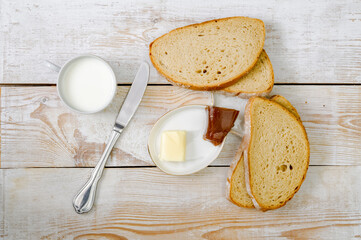 slices of bread, a stylish knife, a cup of milk, butter and quince marmalade on a saucer on a woody rustic table