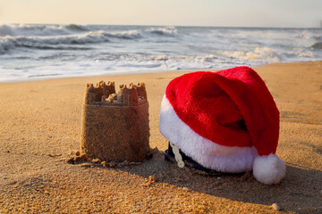 Christmas Santa Claus hat with sand castle on beautiful tropical sandy beach in sea shore at sunset...