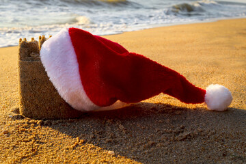 Christmas Santa Claus hat with sand castle on beautiful tropical sandy beach in sea shore at sunset...