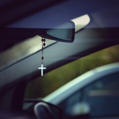Kette mit christlichem Kreuz hängt als Glücksbringer am Rückspiegel im Auto