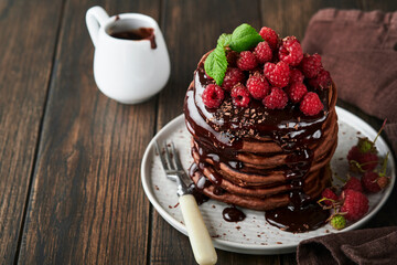 Chocolate Pancakes. Pancakes with fresh raspberry with chocolate glaze or toppings in gray bowl on old wooden table background. Homemade classic american pancakes. Page for magazine concept.