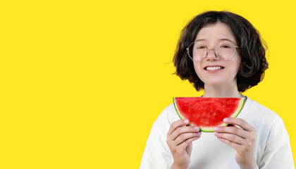 teenage girl in funny glasses holds in her hand piece of juicy ripe watermelon on colored background, copy space