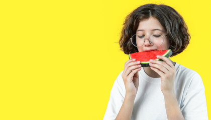 teenage girl in glasses eats piece of juicy red watermelon on colored background, copy space