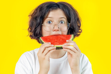 funny teenage girl with glasses with surprised look and wide-open eyes eats piece of juicy red watermelon on colored background