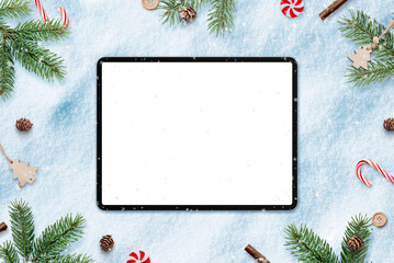 Fototapeta na wymiar Tablet in snow for app design or copy promotion. Surrounded by Christmas decorations. Top view, flat lay