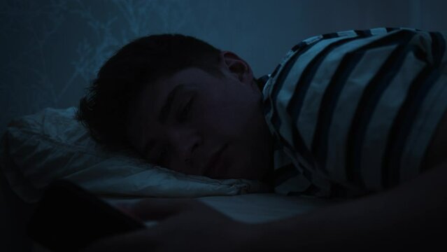 Tired man scrolls on smart phone late at night in bed