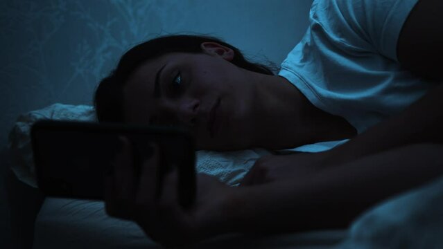 Woman struggles to keep her eyes open whilst using a smart phone in bed