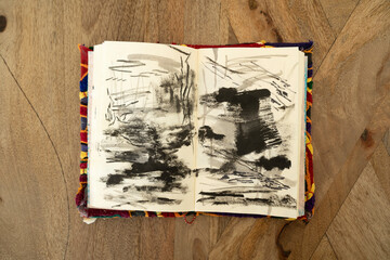 Abstract and expressive art. Top view of an artist's notebook with modern non figurative black and white drawings on the wooden table.