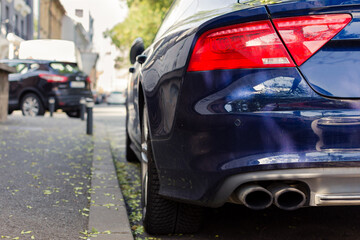 Double exhaust pipe of a modern blue sport car parked next to sidewalk