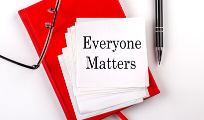EVERYONE MATTERS text on sticker on red notebook with pen and glasses