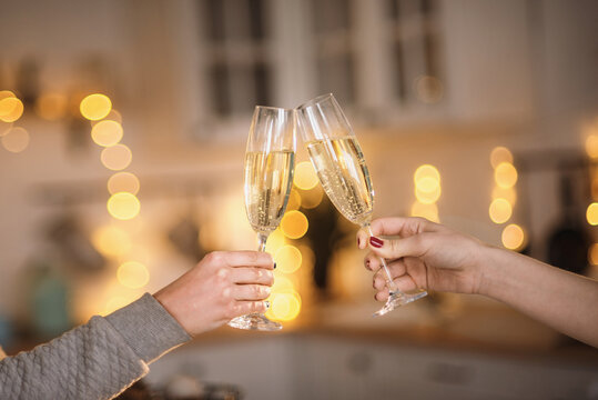 Two women clink glasses with champagne close-up of hands against the backdrop of a Christmas tree and Christmas lights. Lesbian couple celebrating. Women's hands hold thin crystal glasses against the 