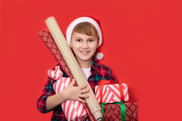Cute caucasian kid teenager boy in Santa hat holds gift boxes with wrapping papers on red background. Copy space for design or text. Banner. Christmas New Year mockup template.