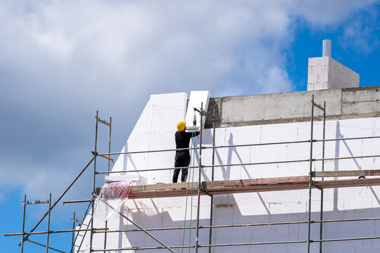 Man installing styrofoam sheets on house facade wall for thermal protection